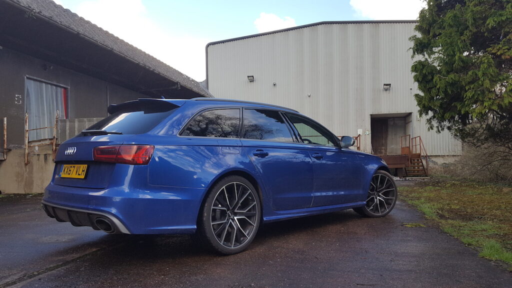 Side view of a blue Audi RS6 outside warehouse buildings