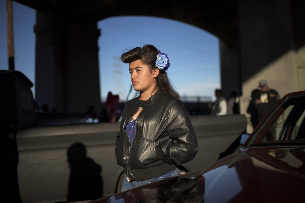 A girl in a leather jacket, with a flower in her hair, looks into the distance.